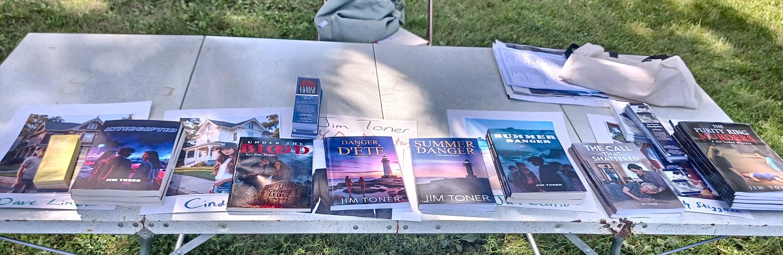 Jim Toner's book signing table at the Better Off Read Festival, showing paperback copies of his mystery and young adult novels.